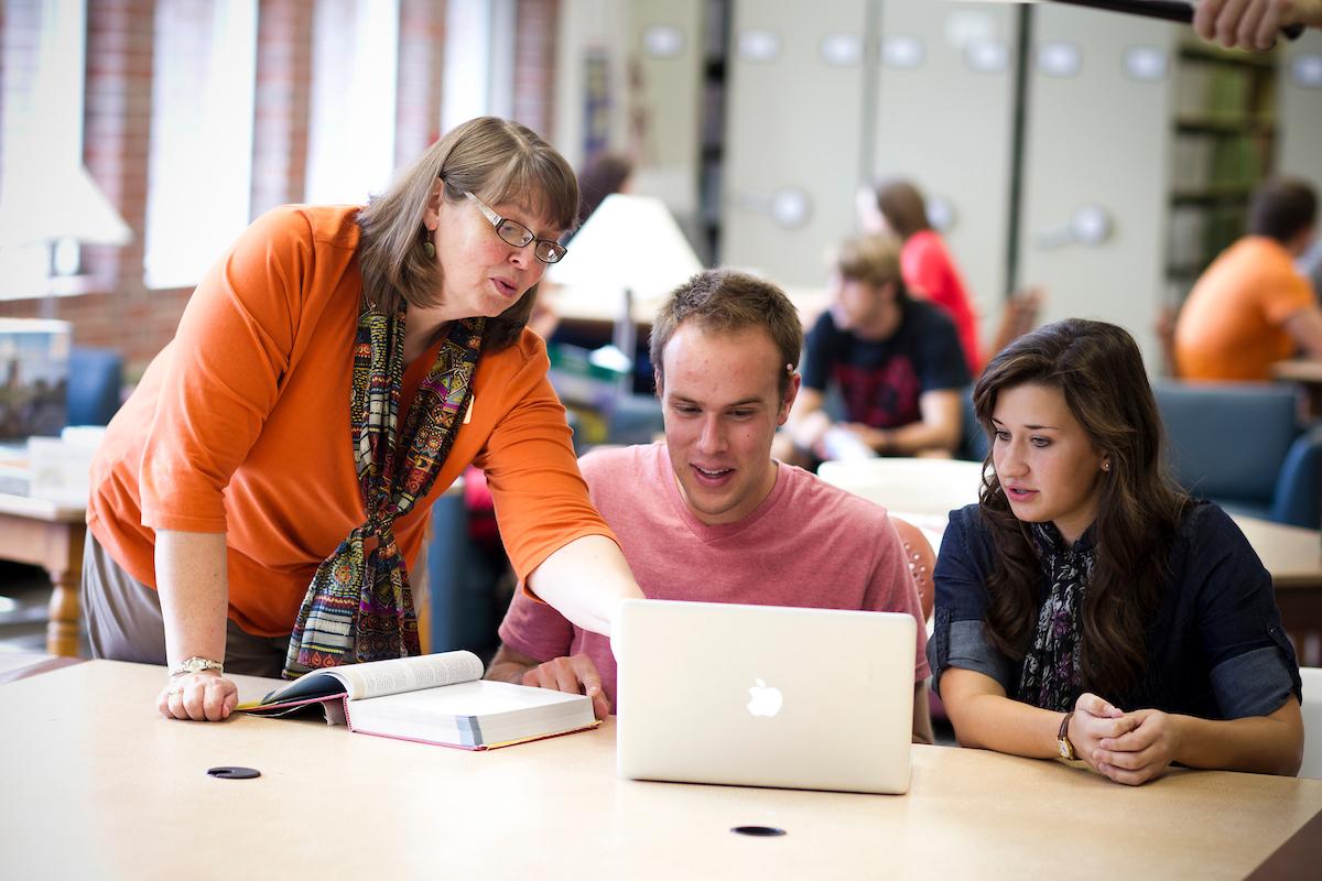 Doane teacher gesturing at a computer while two students watch